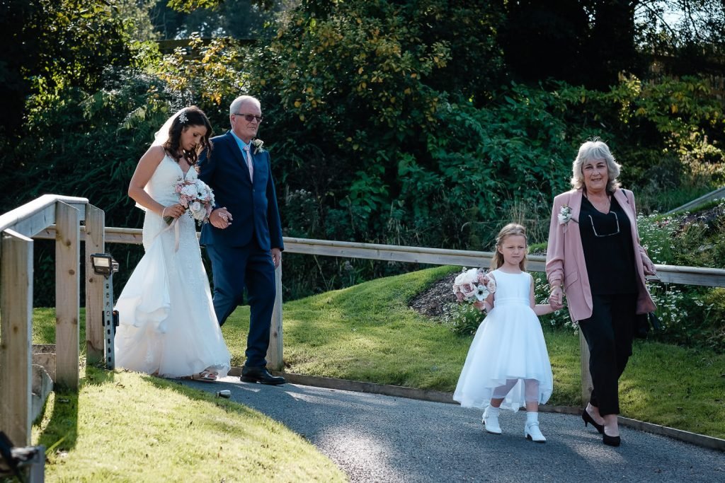 bride walks down the ailse arm in arm with her father. The sun shines behind them- sandy cove elopement wedding